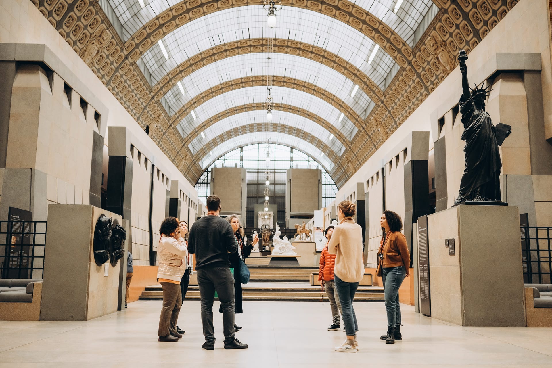  small group of people taking a guided tour inside the Musée d'Orsay, standing near a statue of Liberty.