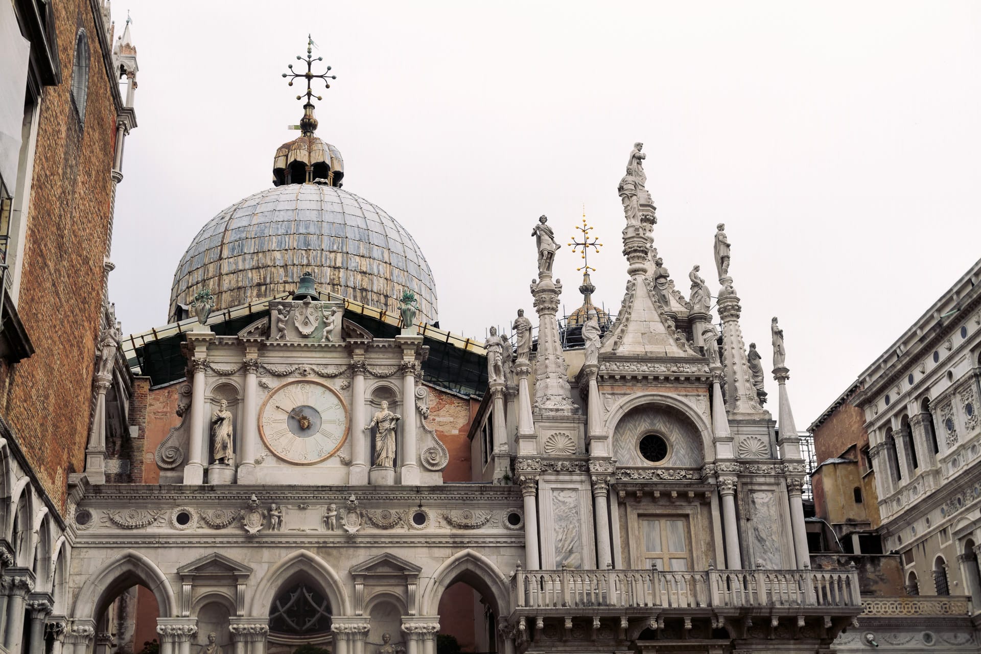 A stunning view of the domes and statues of the Doge’s Palace and Saint Mark’s Basilica, featuring a historical clock face and ornate marble carvings.