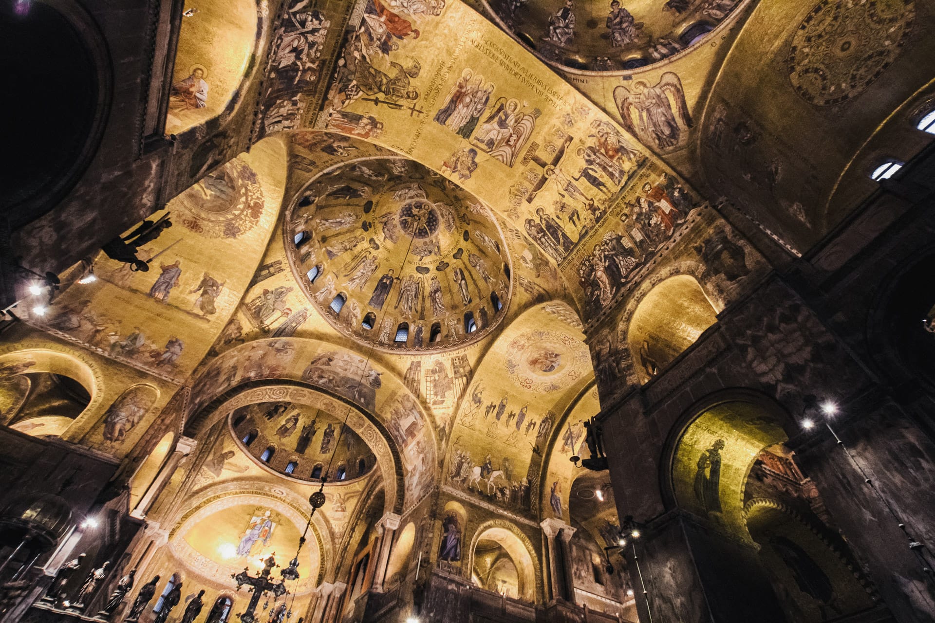 A richly decorated ceiling of a basilica with golden mosaics, religious iconography, and domes featuring intricate biblical scenes and saints.