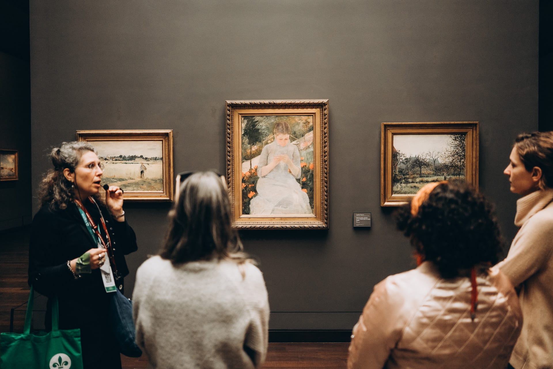  A tour guide explains artwork to a small group of visitors at the Musée d'Orsay, standing in front of paintings by Pierre-Auguste Renoir.