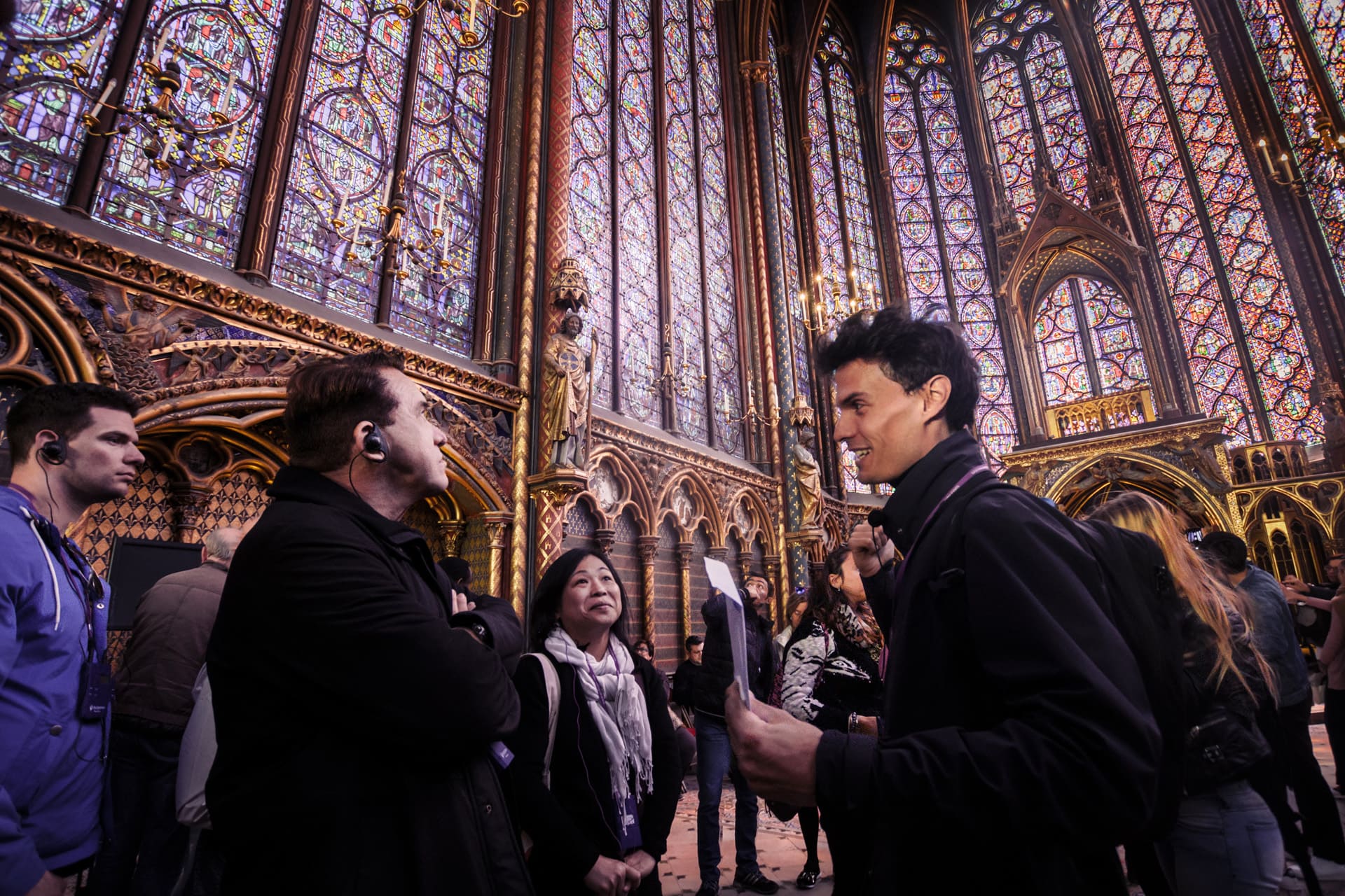 our guide speaking to a group of visitors inside a Gothic chapel with ornate stained glass windows and golden architectural details, as light filters through the colorful glass.