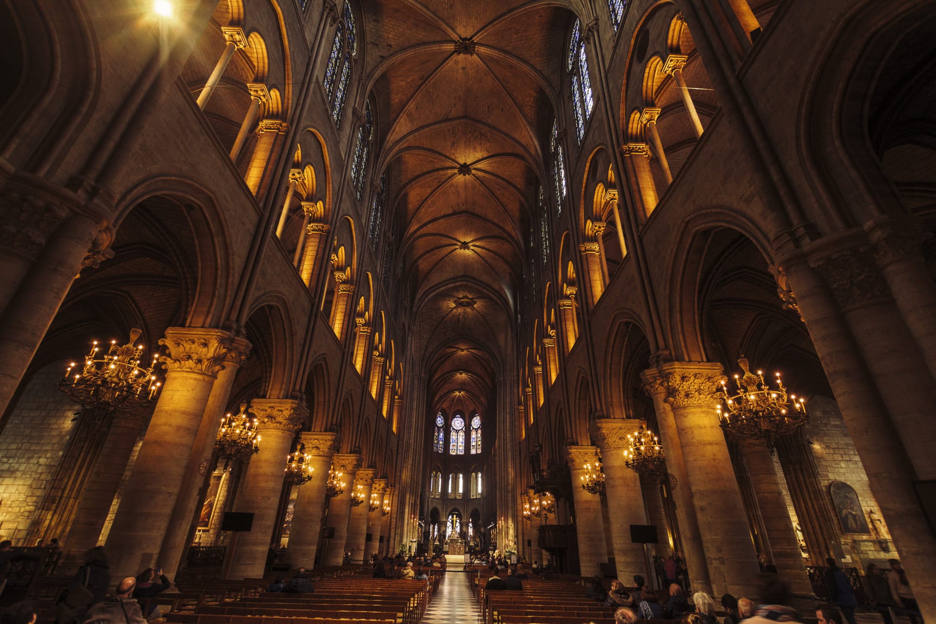 nterior view of a grand Gothic cathedral with towering stone columns, vaulted ceilings, and warm golden lighting, leading the eye toward the altar and stained glass windows at the far end.