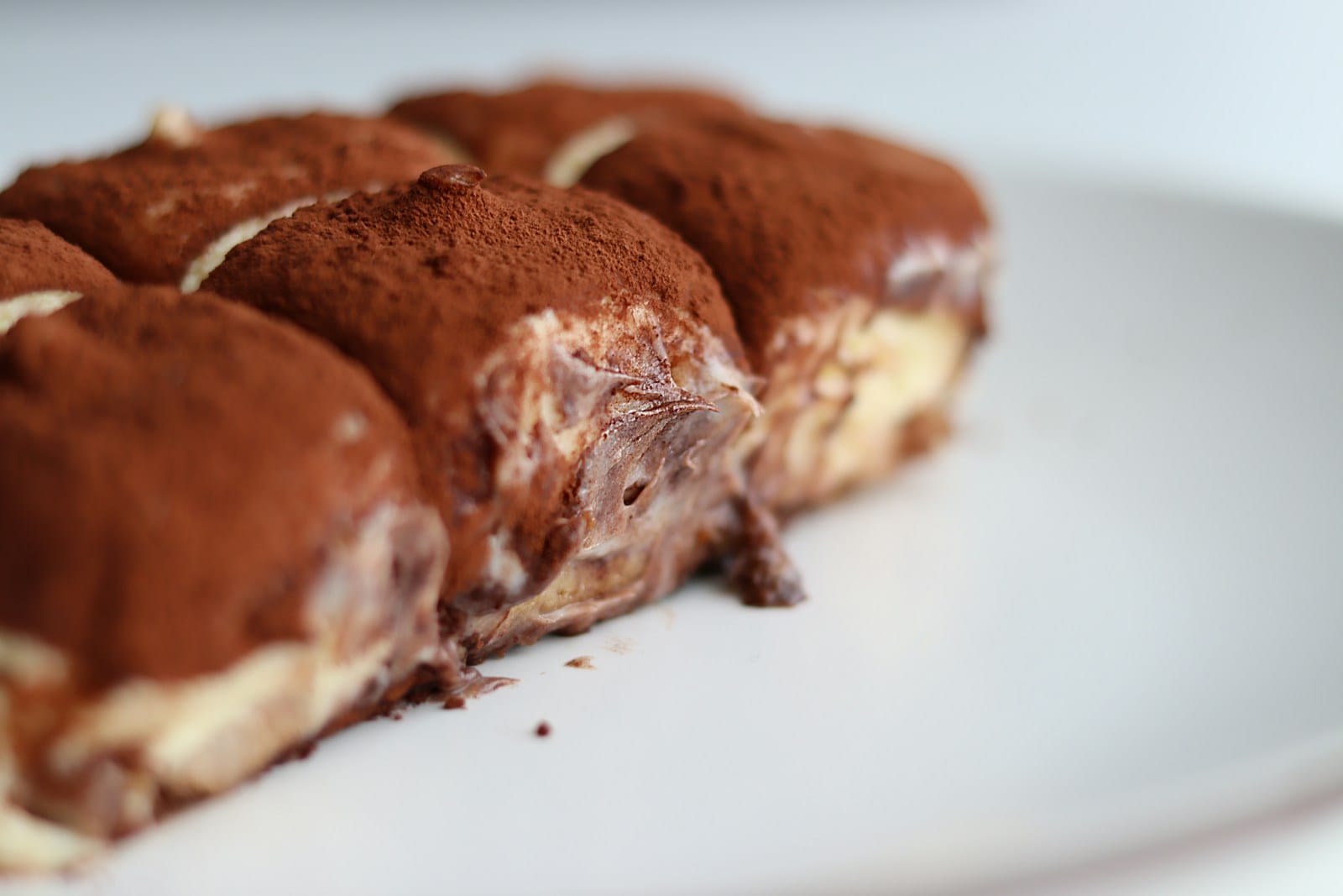 close-up of a delicious-looking tiramisu dessert. The soft layers of creamy mascarpone filling are visible between layers of soaked ladyfingers, topped with a dusting of cocoa powder.