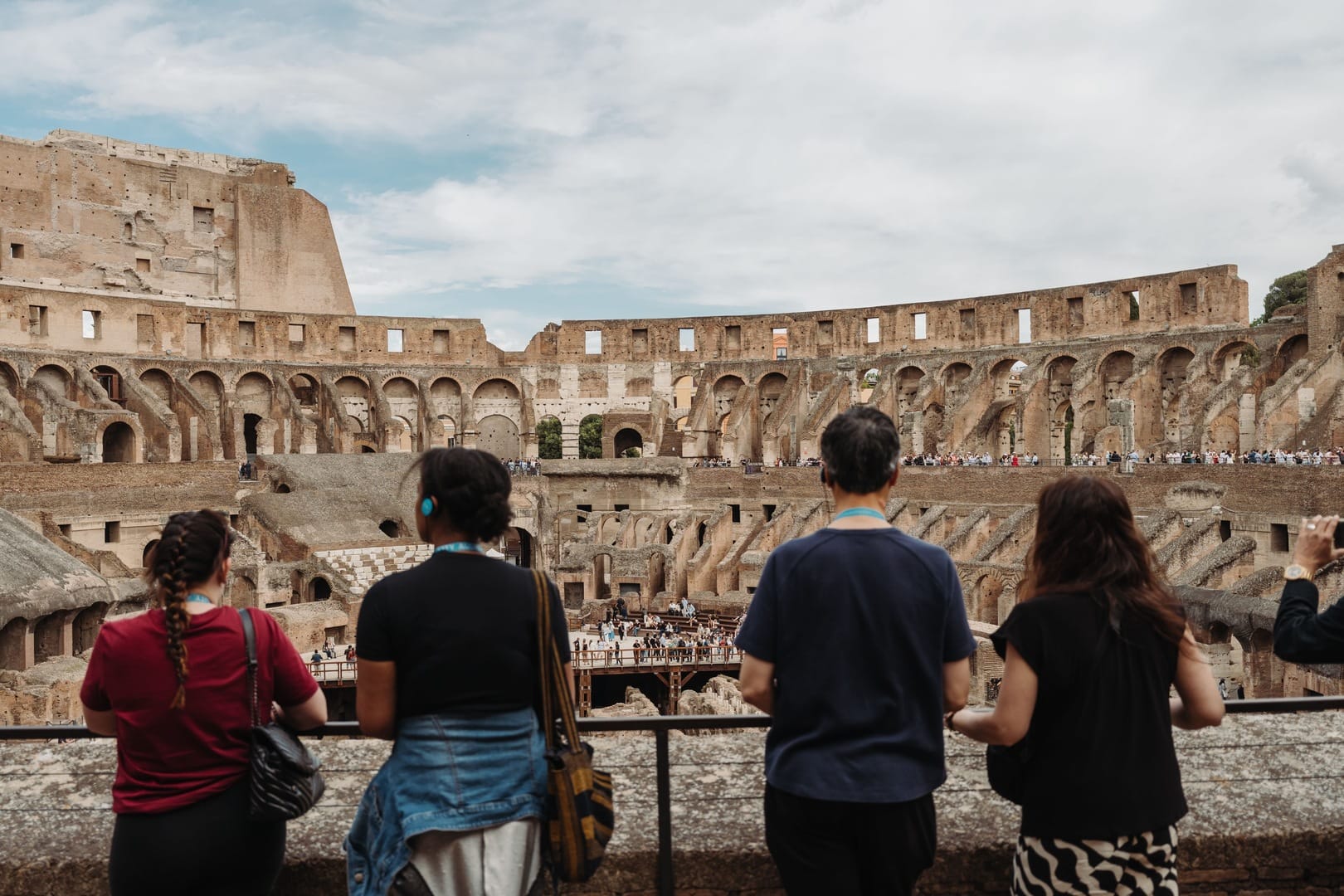 Four tourists view the impressive interior walls of the Colosseum, while listening to an audio tour on headphones.