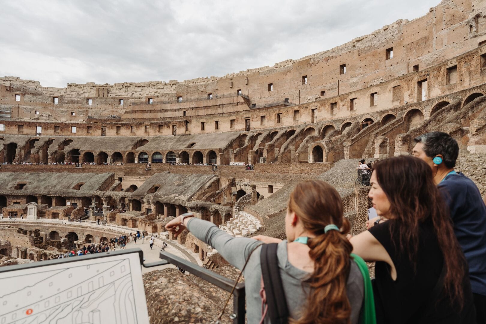 a tour guide pointing to the arena area of the colosseum from one of the stands, with a couple on a private guided tour