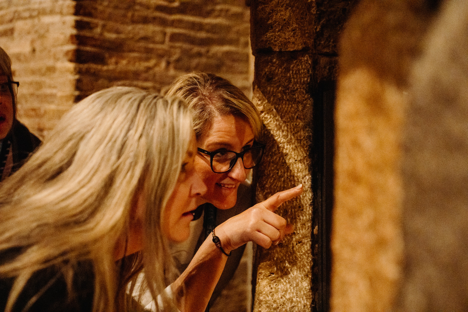 a closeup of 2 women pointing and looking through an archway in the brick-lined underground tunnels of the catacombs in Rome
