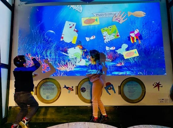 2 young children playing in front of an interactive exhibit that looks like a giant aquarium in the museo de bambini in Rome 