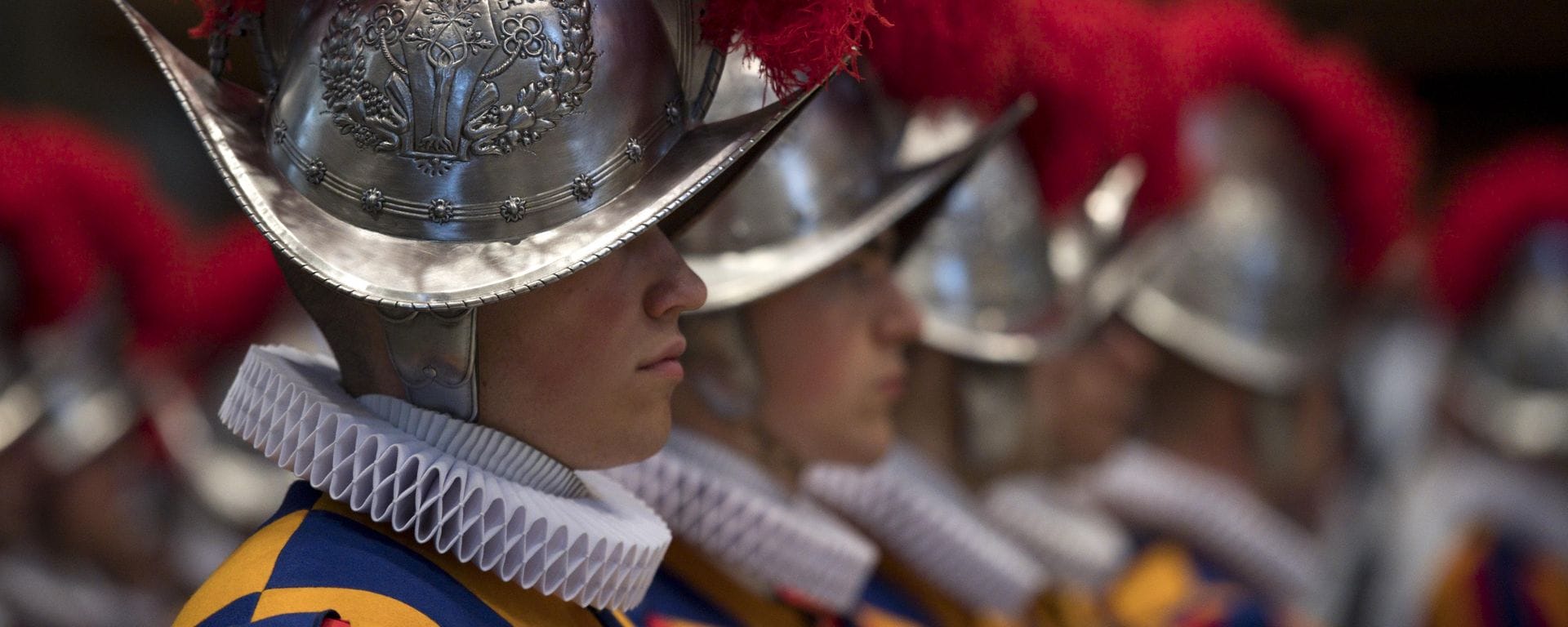 A close up of the head and shoulders of a Swiss guard stood in line with his colleagues