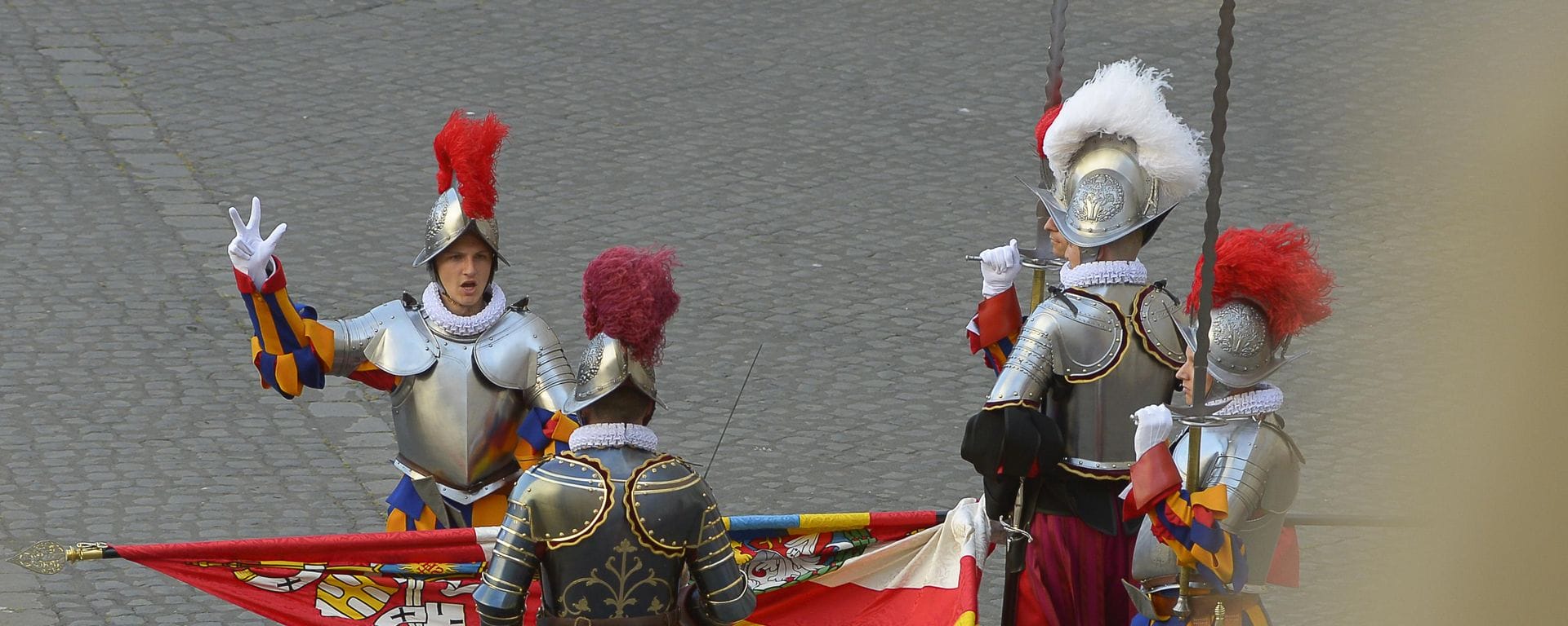 Why does the Vatican have Swiss guards? a group of swiss guards in traditional red yellow and blue uniform with silver armour and plumed helmets