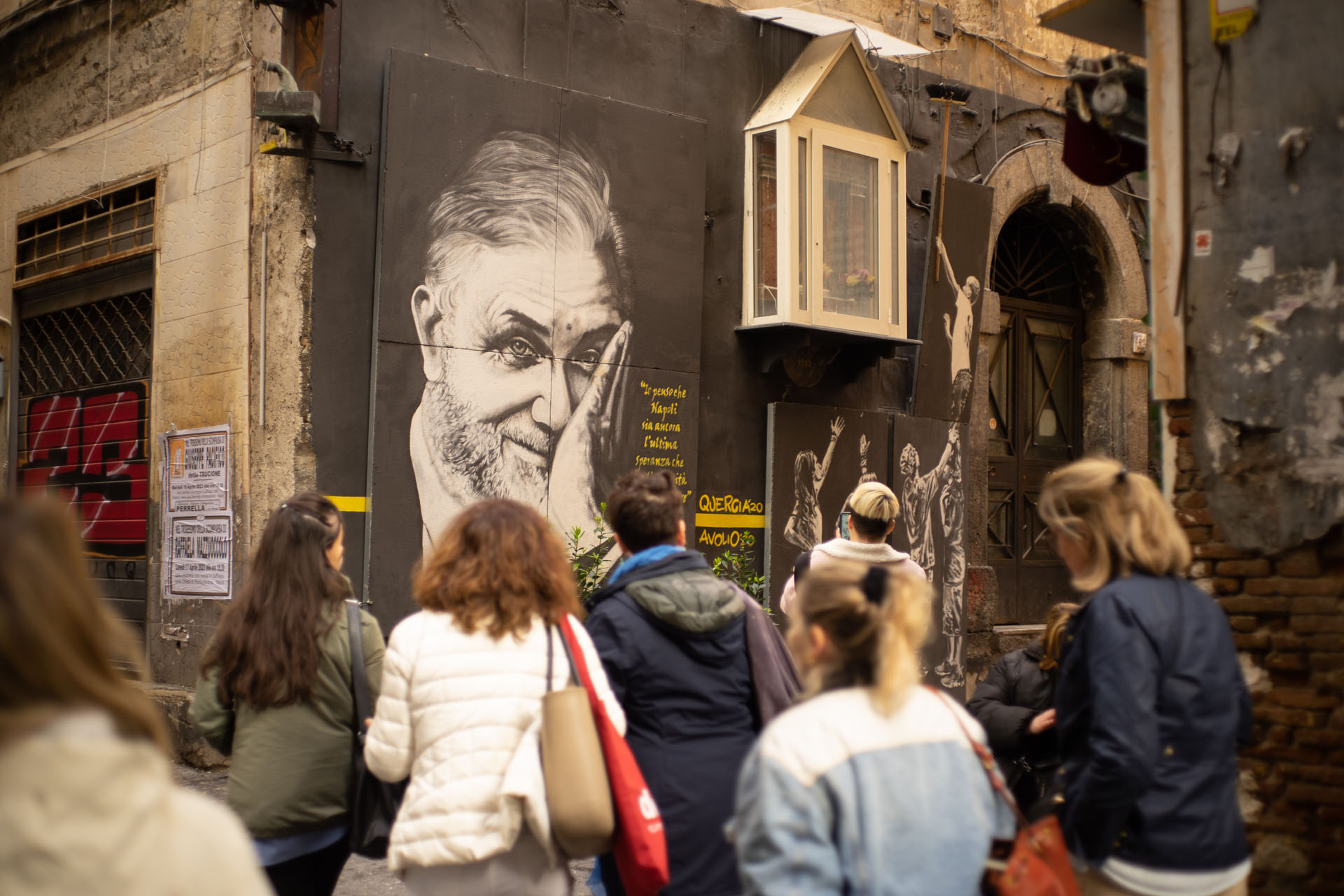 A group fo visitors look at a painted mural on the walls of the Quartieri Spagnoli - spanish quarter - in Naples